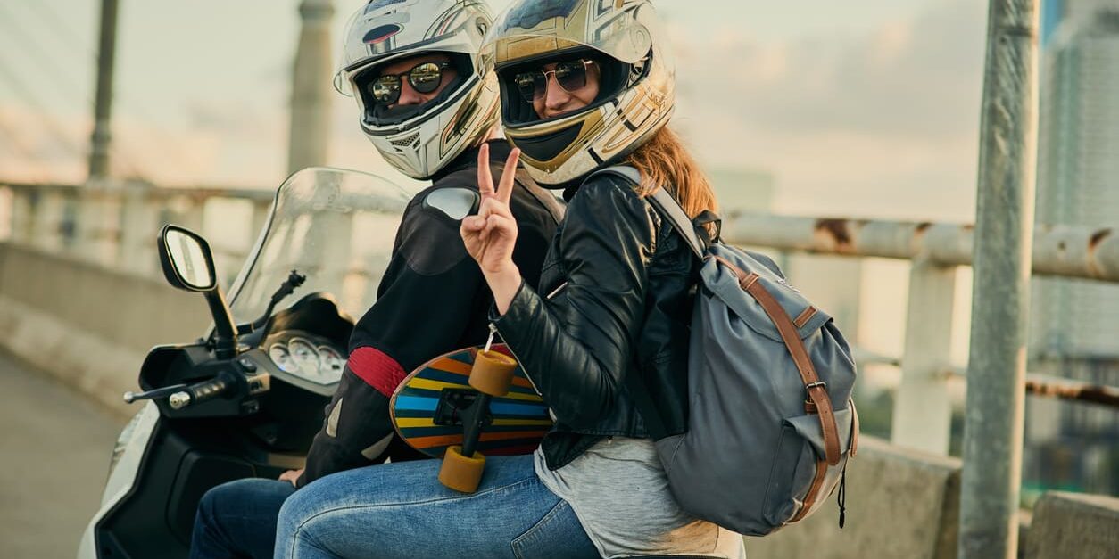 llevar-pasajero-moto-novel-normativa-dgt Una pareja de moteros equipados saliendo de ruta en una motocicleta con la placa L de conductor novel, demostrando que sí se puede llevar pasajero.