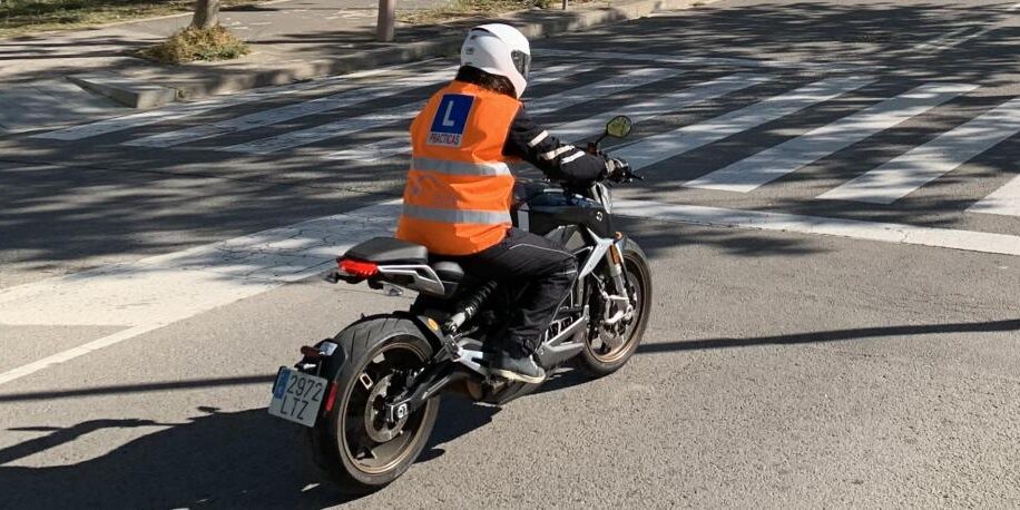 Motorista de la autoescuela MotoCircuito realizando prácticas de circulación en ciudad, seguido de cerca por el coche del profesor en Móstoles.