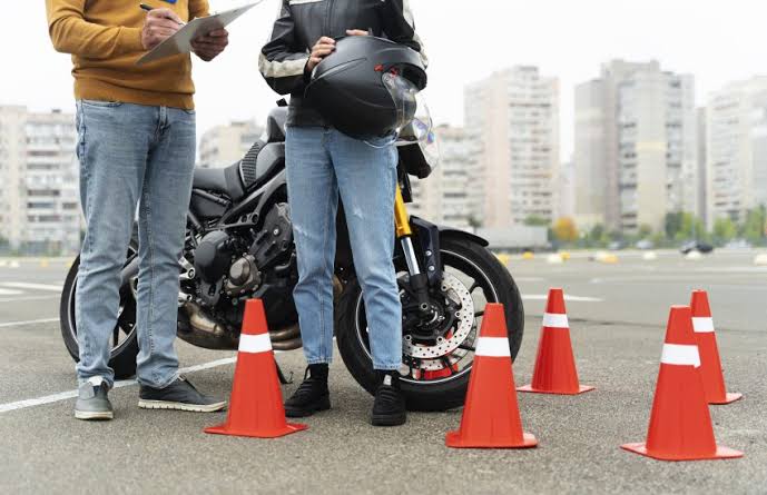 Alumno de la autoescuela MotoCircuito sonriendo y mostrando la placa de la 'L' junto a su profesor en Móstoles, celebrando la obtención de su carnet de moto A2 en tiempo récord.