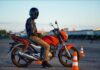 Motorista de la autoescuela MotoCircuito detenido correctamente ante una señal de STOP con un pie apoyado en el asfalto durante una práctica de circulación en Móstoles, seguido por el coche del examinador.
