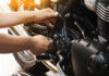 Detalle de un motorista aplicando grasa de mantenimiento en la cadena de su motocicleta nueva, aplicando los consejos aprendidos en la autoescuela MotoCircuito.