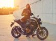 Una alumna sonriente de la autoescuela MotoCircuito equipada con casco y chaqueta, sentada con seguridad sobre una motocicleta de prácticas en el circuito de Móstoles.