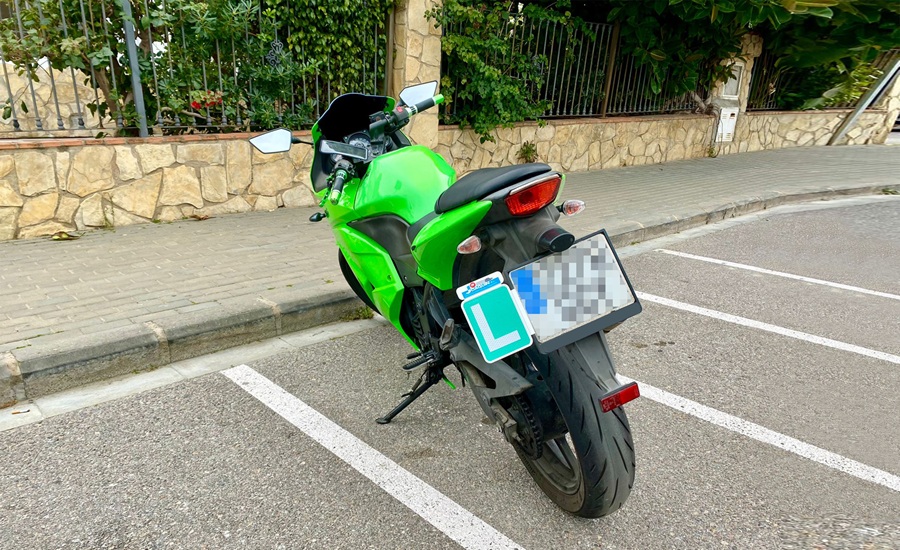 Detalle de la parte trasera de una motocicleta con la placa 'L' de conductor novel correctamente instalada mediante un soporte junto a la matrícula.